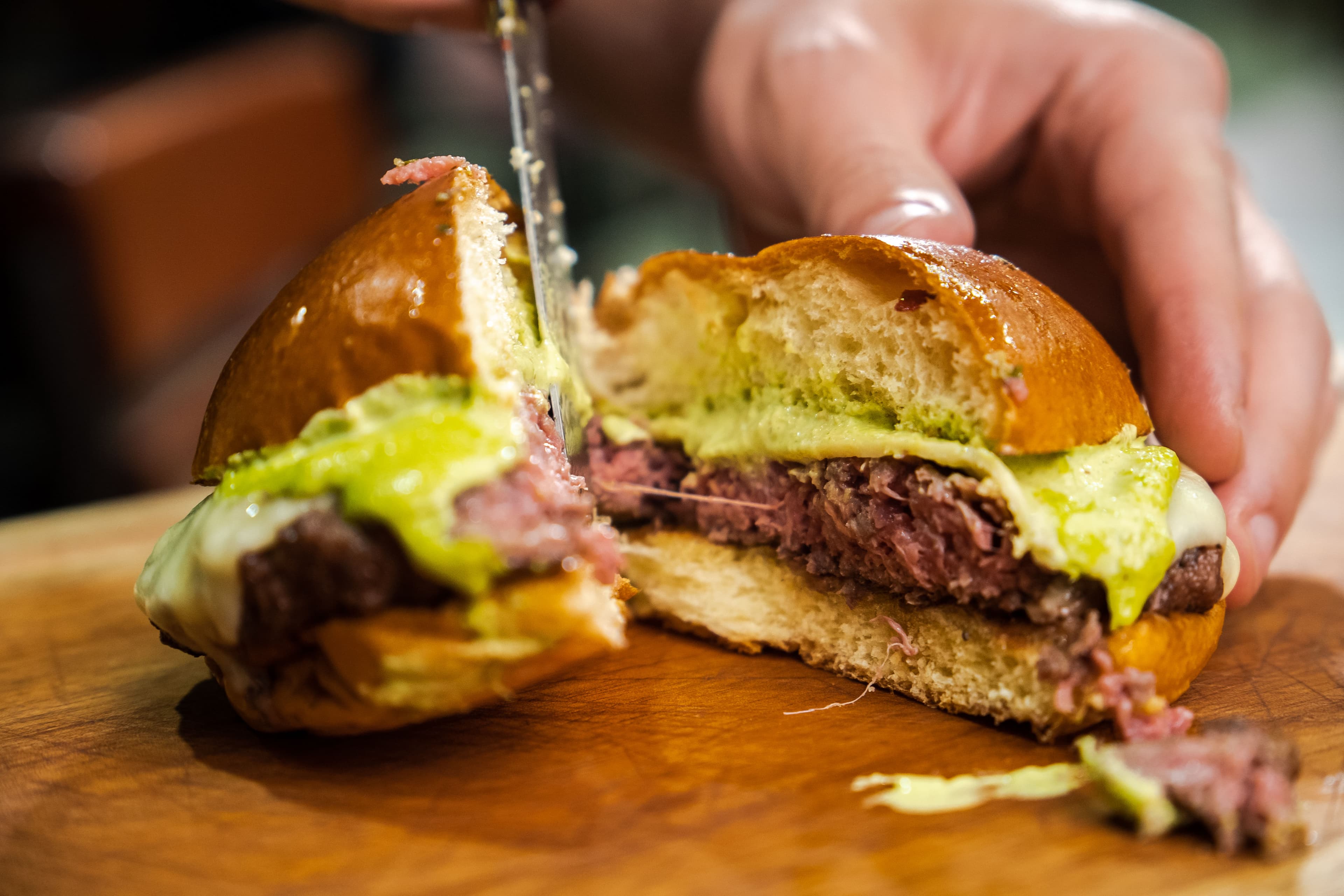 Imagem representando um hambúrguer sendo cortado por uma faca no Planador Parilla e Bar, localizado no Raboni Complexo Esportivo